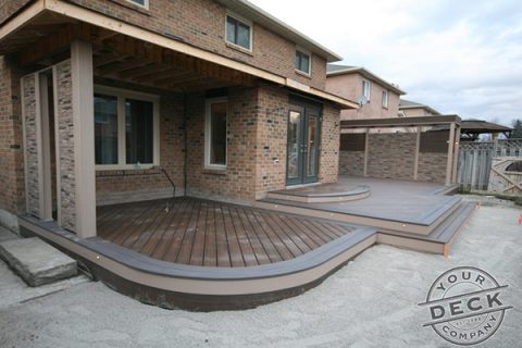Image of a deck with curves and multiple levels. Trex Spiced rum decking and a custom stone privacy wall