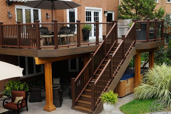 image of an elevated low maintenance deck. There is a hot tub under the deck on a stone patio