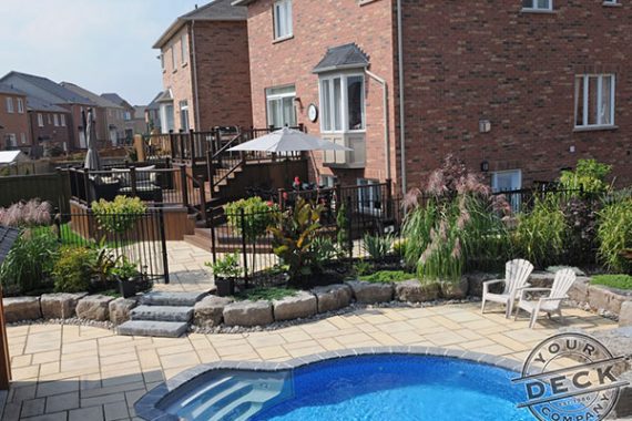 fully finished backyard landscape complete with a deck, stone patio and a pool