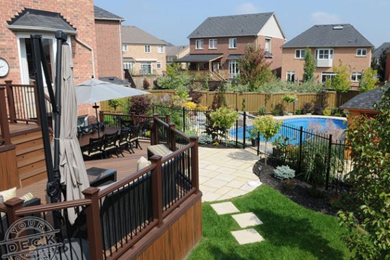 fully finished backyard landscape complete with a deck, stone patio and a pool